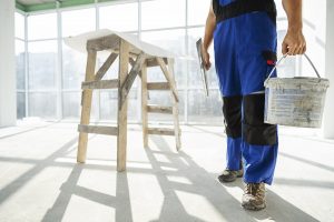 contractor carrying a bucket of paint in an office with large windows