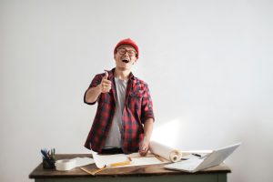 contractor at his work desk filled with blueprints, smiling and giving a thumbs-up